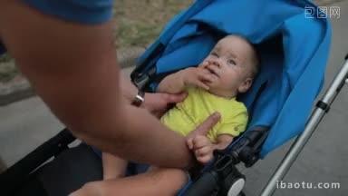 有胡子的帅气潮爸爸从婴儿车里抱起他的婴儿，在一起的时候亲吻